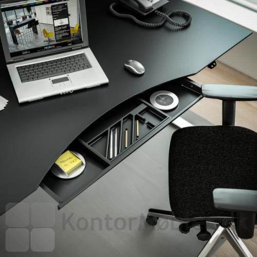 Delta hævesænkebord med sort overflade og udtræksskuffe til opbevaring af kontorartikler og lignende sager som du bruger i løbet af en arbejdsdag.